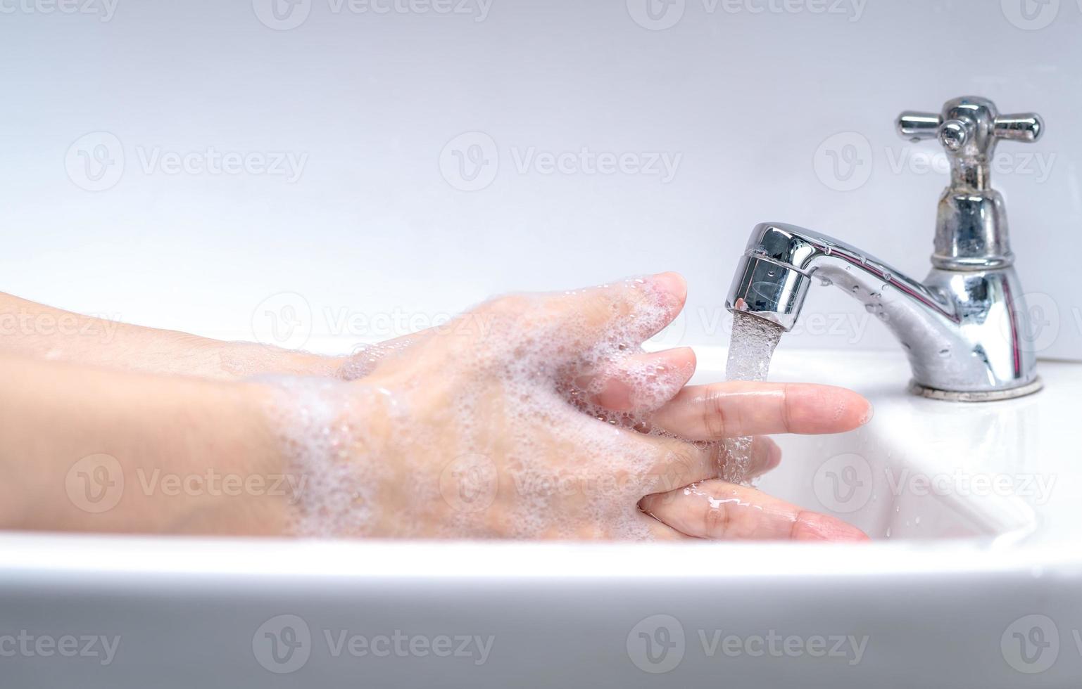 Woman washing hand with soap foam and tap water in bathroom. Hand clean under faucet on sink for personal hygiene to prevent flu and coronavirus. Good procedure of hand wash to kill bacteria, virus. photo