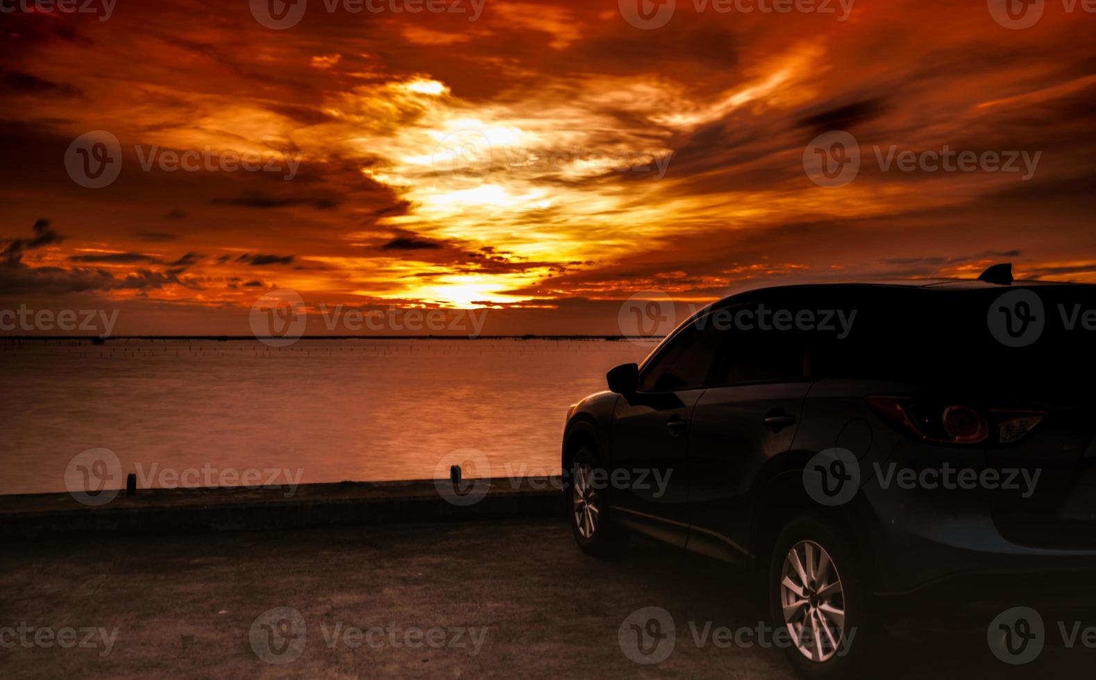 Luxury blue SUV car parked on concrete road by the sea at sunset with dramatic sky and clouds. Electric car technology and business. Hybrid auto and automotive industry. Tropical road trip travel. photo