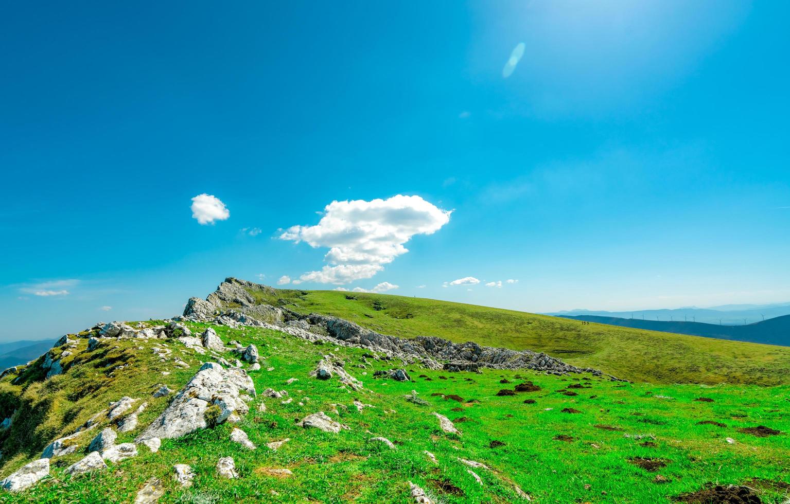 paisaje de hierba verde y colina rocosa en primavera con hermoso cielo azul y nubes blancas. campo o vista rural. fondo de naturaleza en un día soleado. ambiente de aire fresco. piedra en la montaña. foto