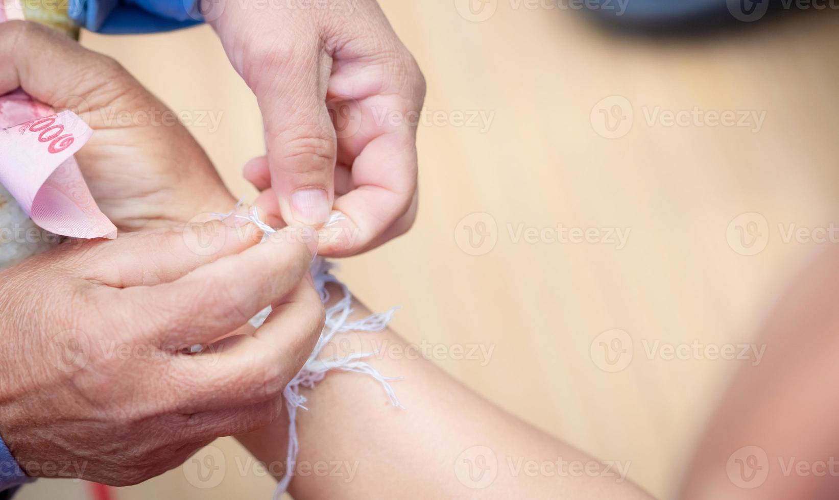 The ceremony of binding people wrist with the holy thread to console people's Kwan. Thai culture. Beliefs and local culture of Northeastern Thai people. Old person binding holy thread to Thai adult. photo