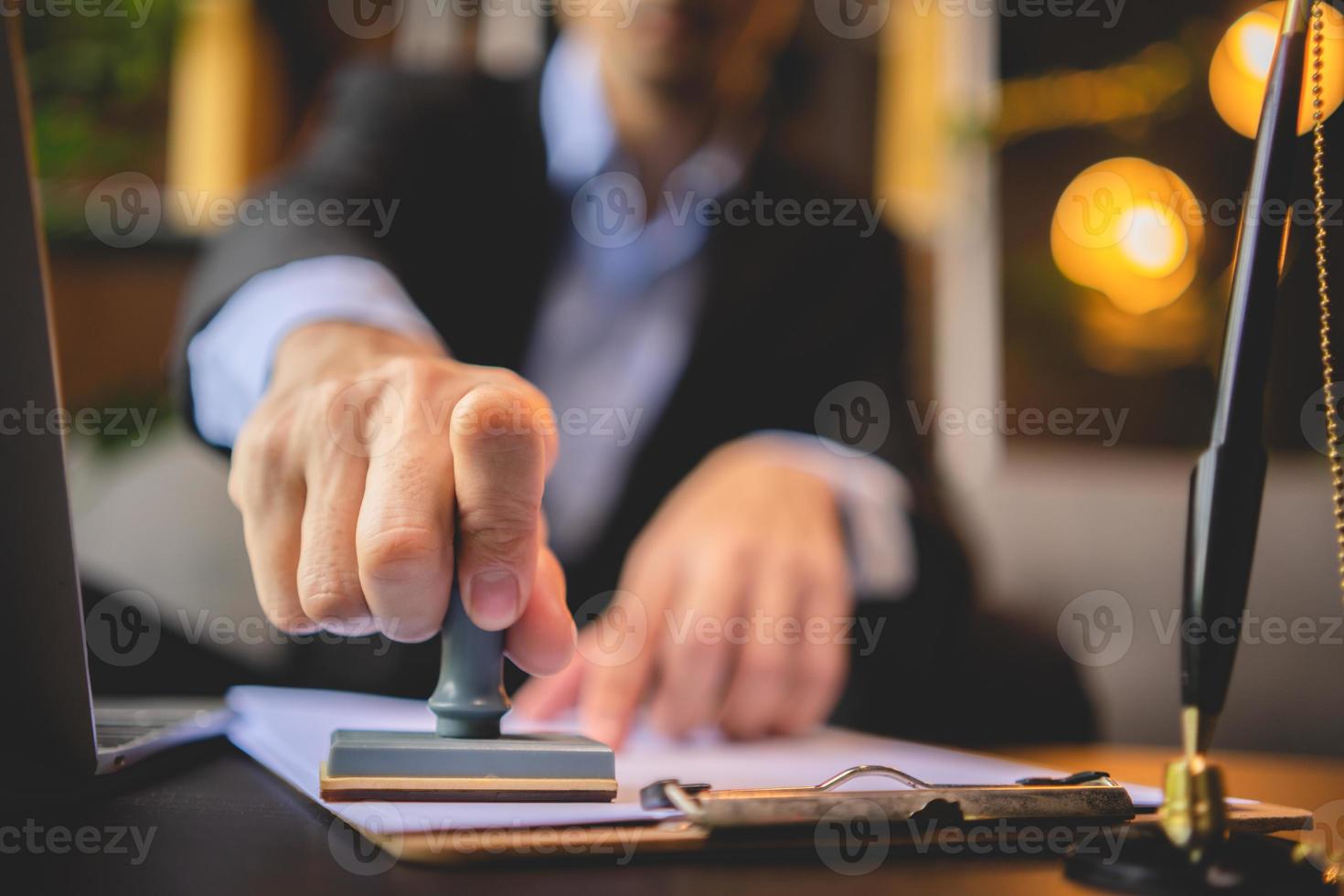 Close-up of a person's hand stamping with approved stamp on approval certificate document public paper at desk, notary or business people work from home, isolated for coronavirus COVID-19 protection photo