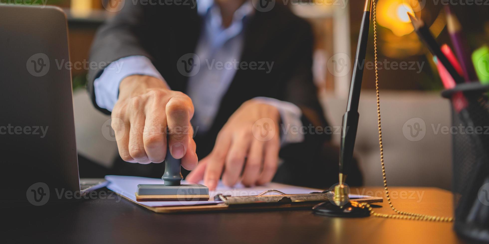 Close-up of a person's hand stamping with approved stamp on approval certificate document public paper at desk, notary or business people work from home, isolated for coronavirus COVID-19 protection photo