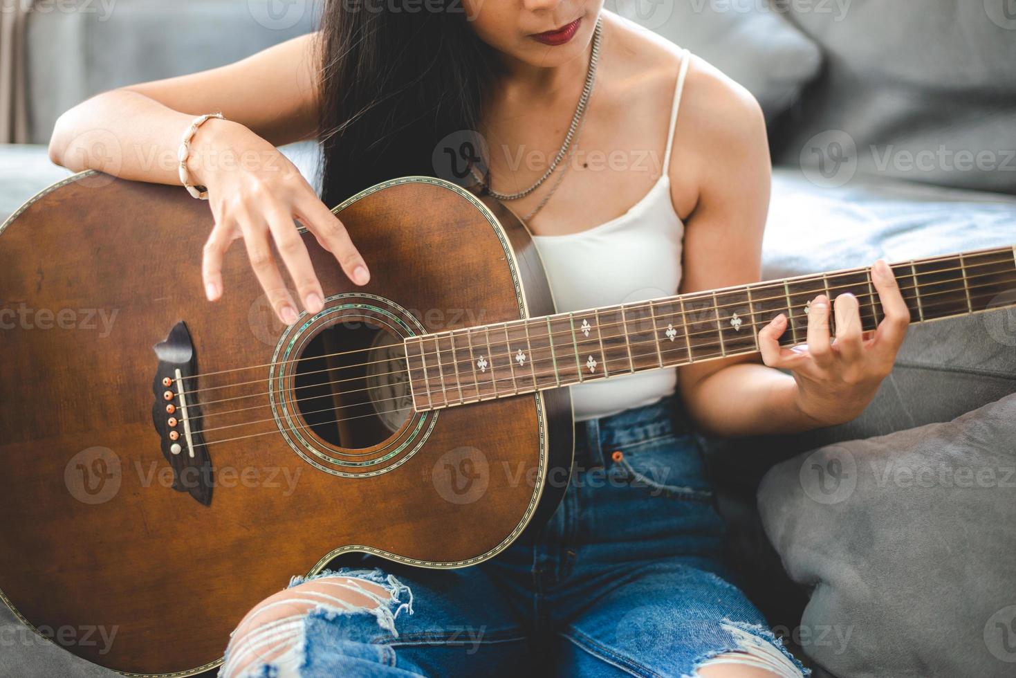 Asian woman playing music by guitar at home, young female guitarist musician lifestyle with acoustic art instrument sitting to play and sing a song making sound in hobby in the house room photo