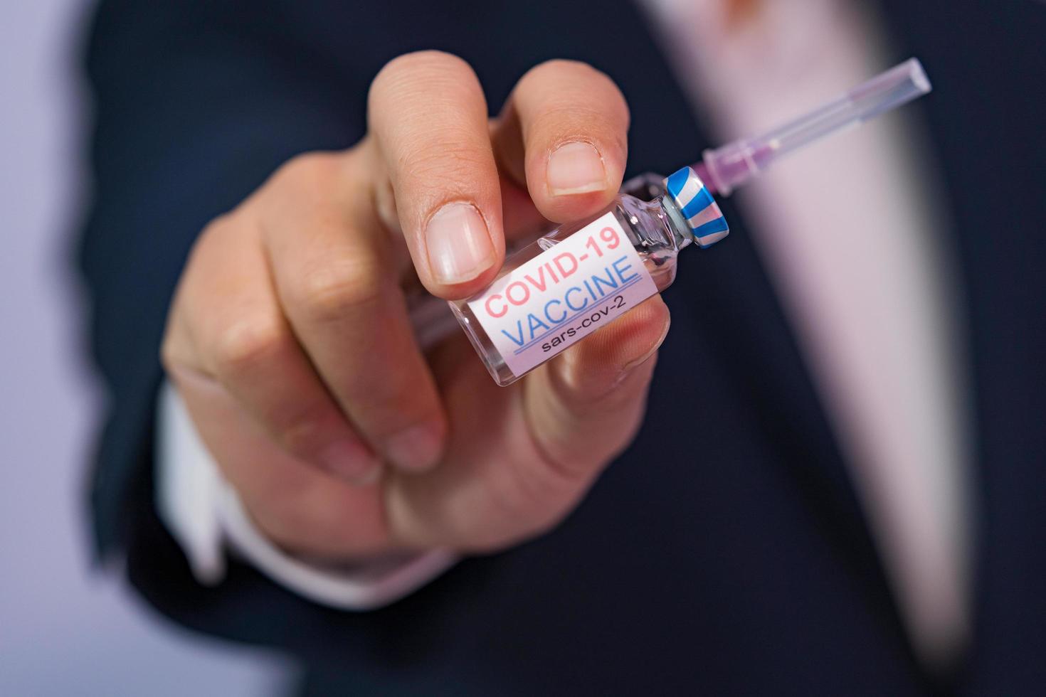 Focus select and blur Foreground Vaccine COVID-19 corona virus and syringe on hand business man in blue suit background. Concept of attentive care. photo