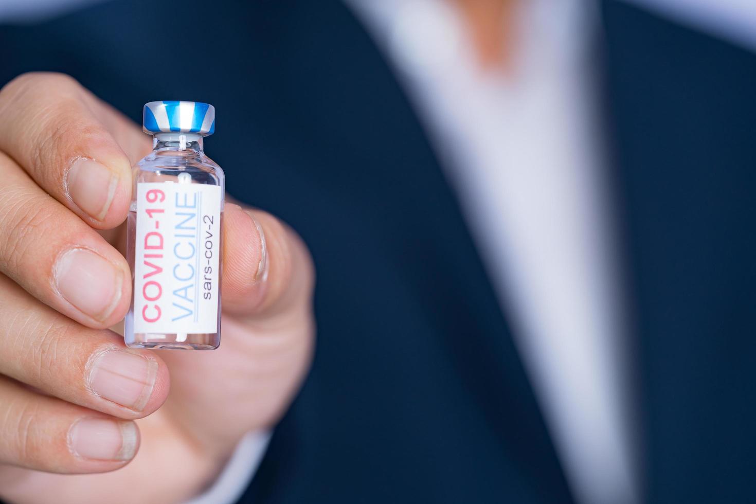 Focus select and blur Foreground Vaccine COVID-19 corona virus and syringe on hand business man in blue suit background. Concept of attentive care. photo