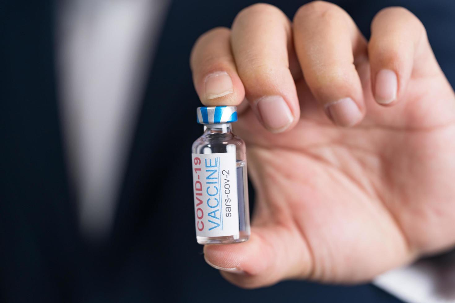 Focus select and blur Foreground Vaccine COVID-19 corona virus and syringe on hand business man in blue suit background. Concept of attentive care. photo
