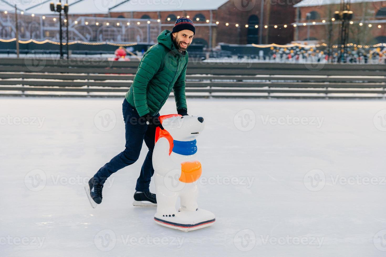 Portrait of glad handsome middle aged male skates on ice rink with skate aid, going to show good results, has pleasant smile, happy to spend spare time on fresh winter air during nice weather photo