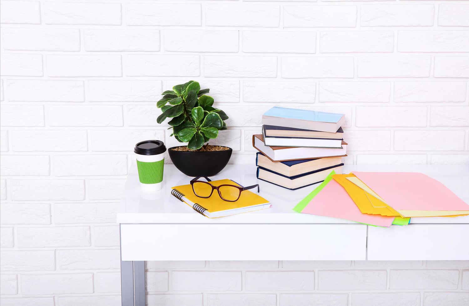 lugar de trabajo con taza de café y material educativo en la habitación. pared de ladrillo. copie el espacio y el enfoque selectivo foto