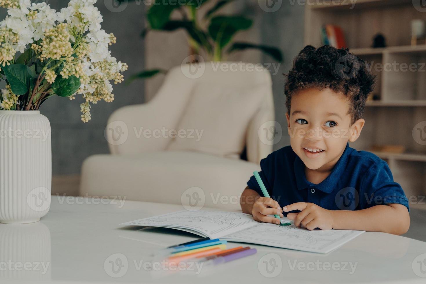 Cute afro american child painting in coloring book at home photo