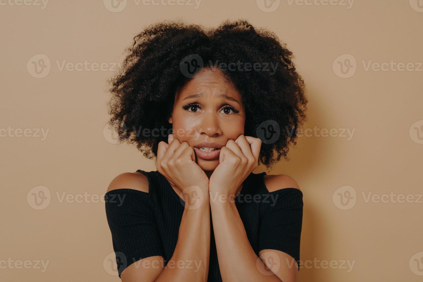 Scared mixed race female looking nervously and feeling stress while posing against beige background photo