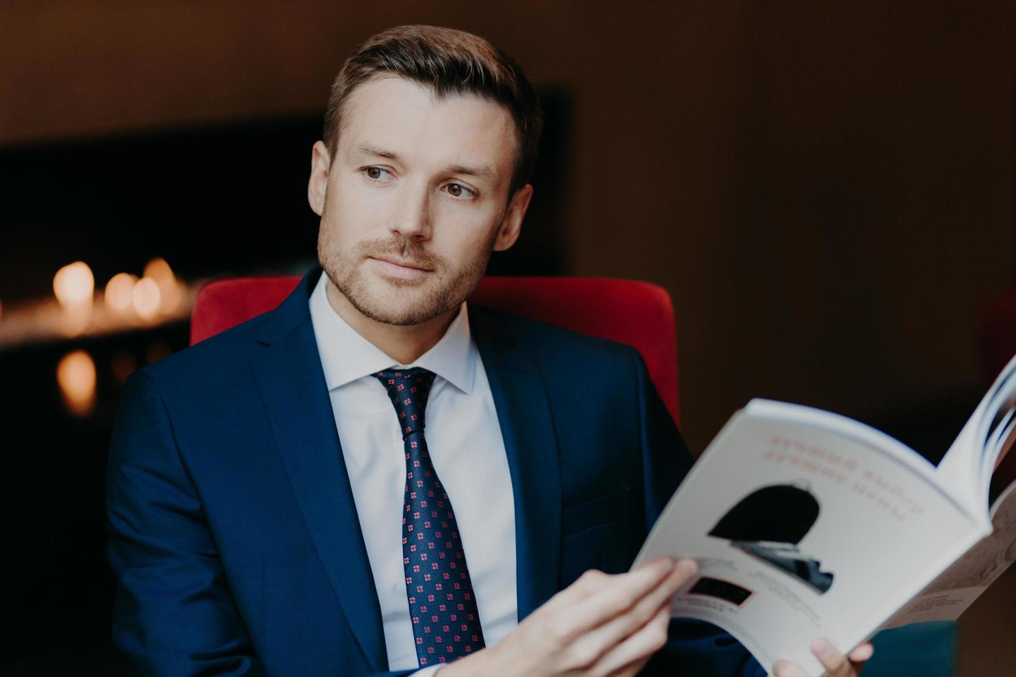 Pensive successful male employee focused into distnace, holds magazine, dressed in formal clothes, waits for business partner in cafe, thinks about signing contract and collaboration. People and work photo