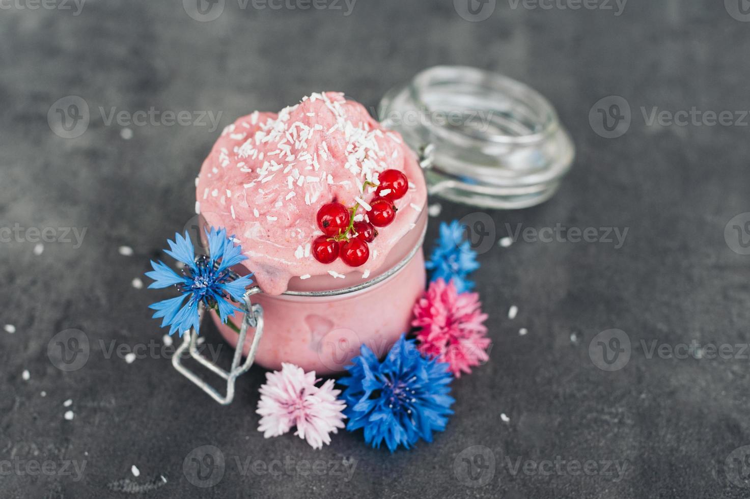 Delicious strawberry ice cream decorated with coconut flakes, red currant and blue cornflowers against grey background. Tasty dessert. Food concept photo