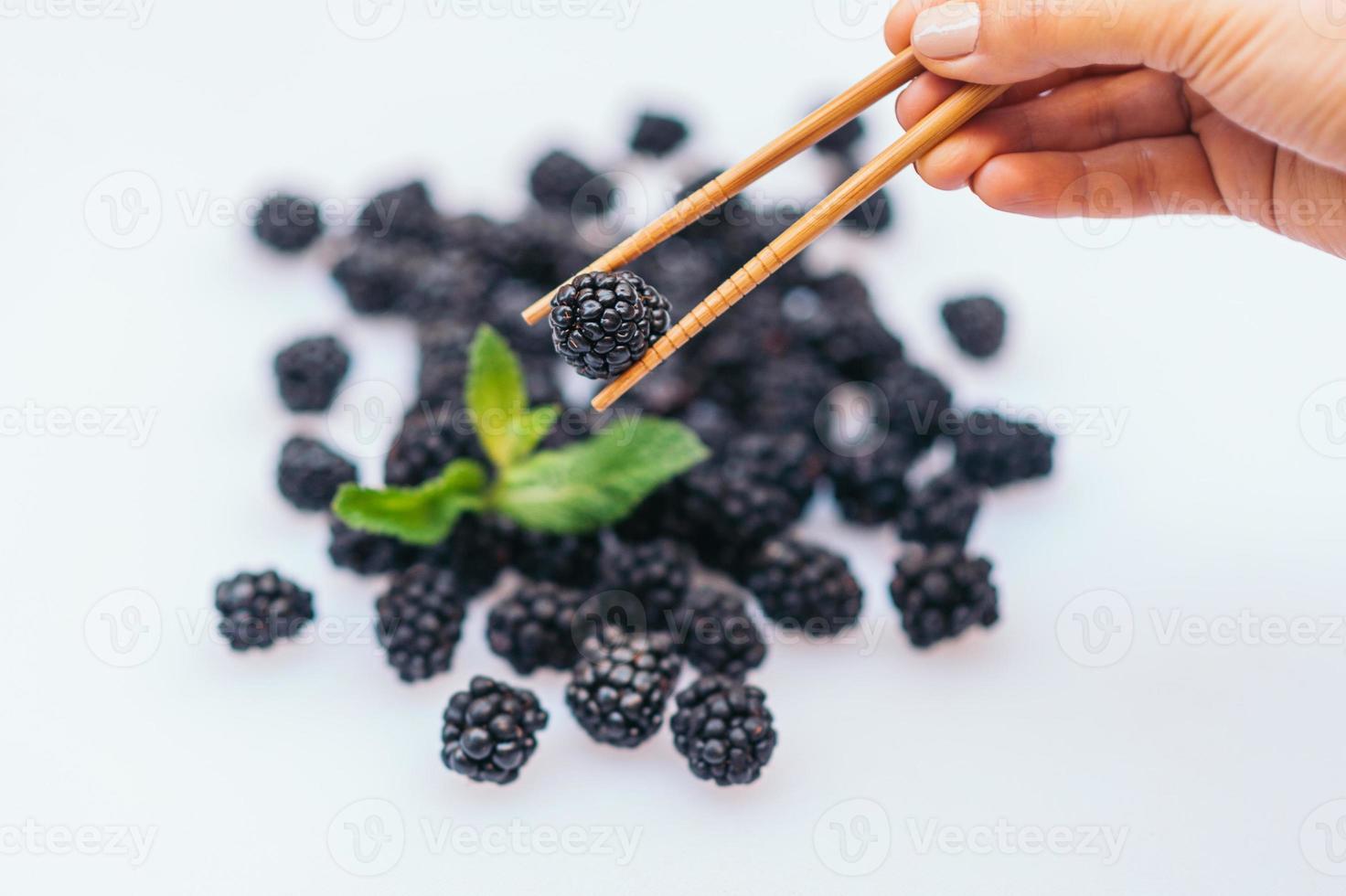 Fresh ripe balckberry with mint against white background. Unknown person holds chopsticks with fresh berries. Vegan food. Healthy nutrition concept. Eat for planet photo