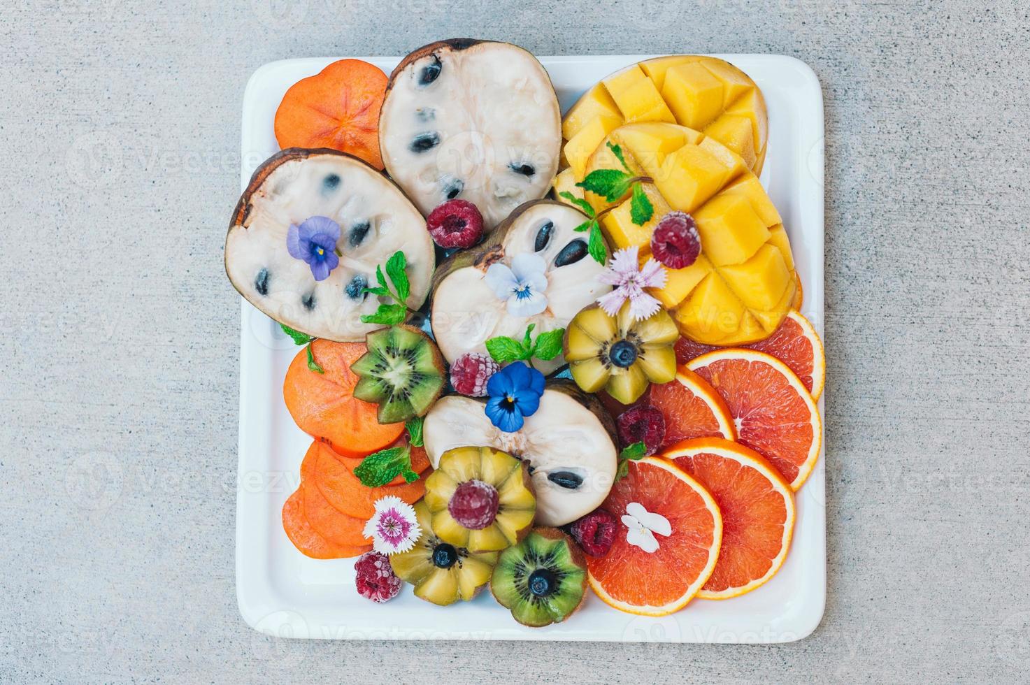 Flat lay of exotic tropical fruits. Gold kiwi, persimone, raspberry, mango, oranges and mint. Plate of fresh decorated craved ripe fruits. Food concept photo