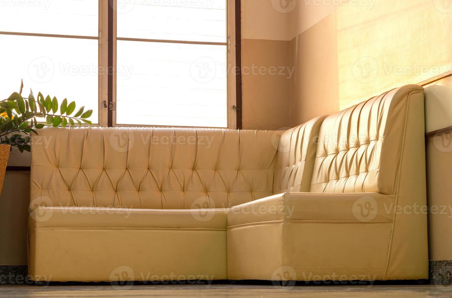 Old cream-colored sofa in the corner of the room with window light. photo