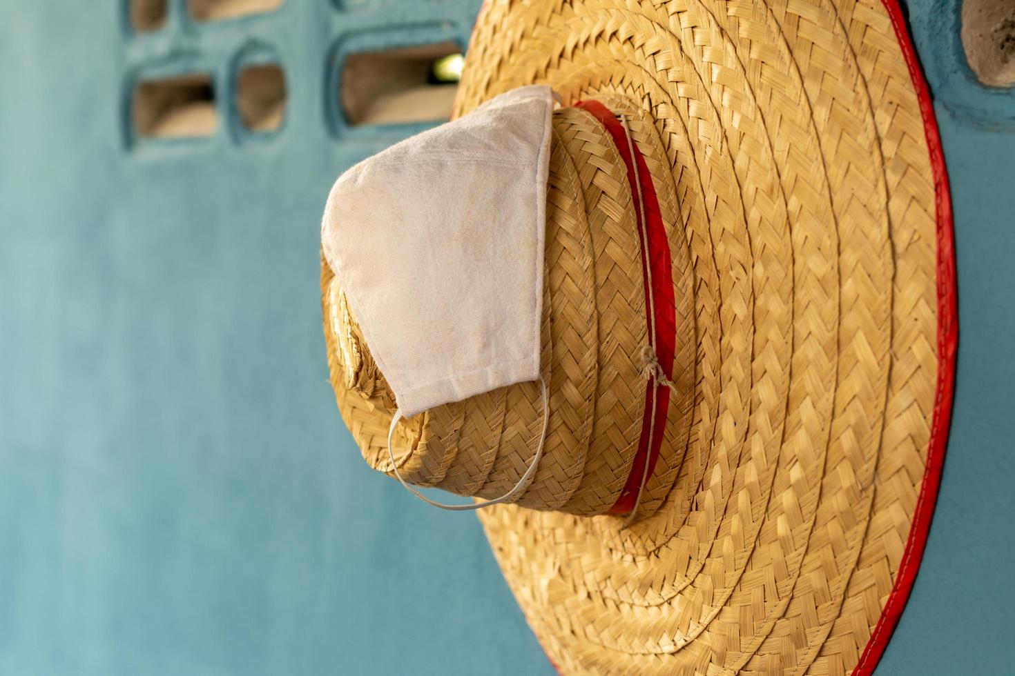 sombrero de bambú tejido con una máscara colgada en una pared de hormigón. foto