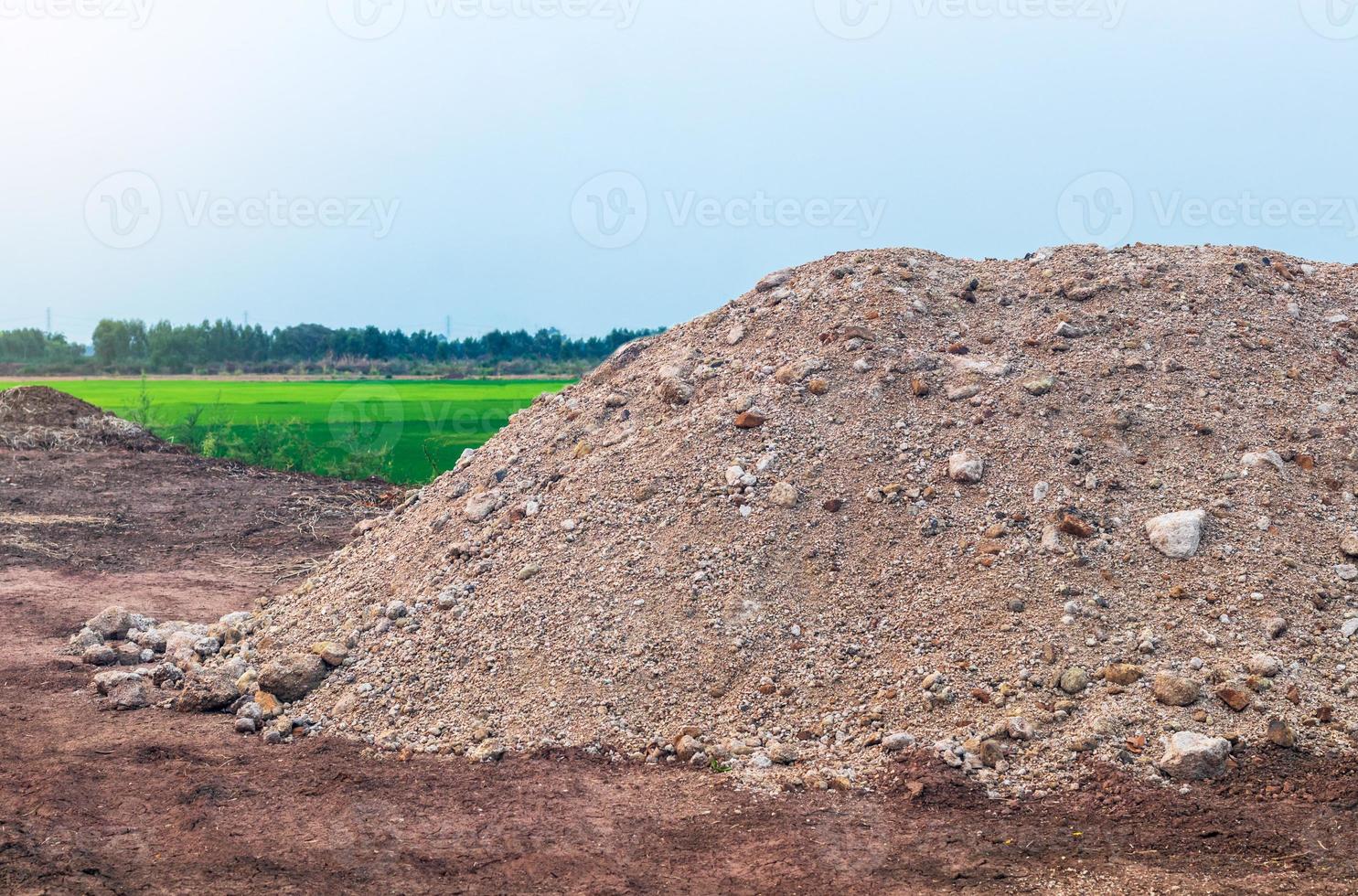 A pile of gravel sand and green rice fields. photo