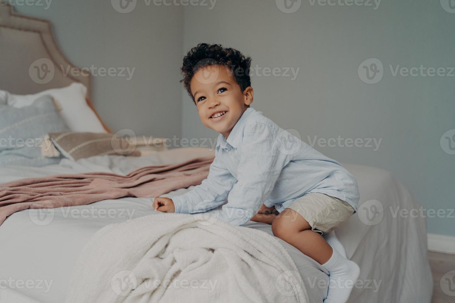 Cute young afro american boy playing on big bed at home photo