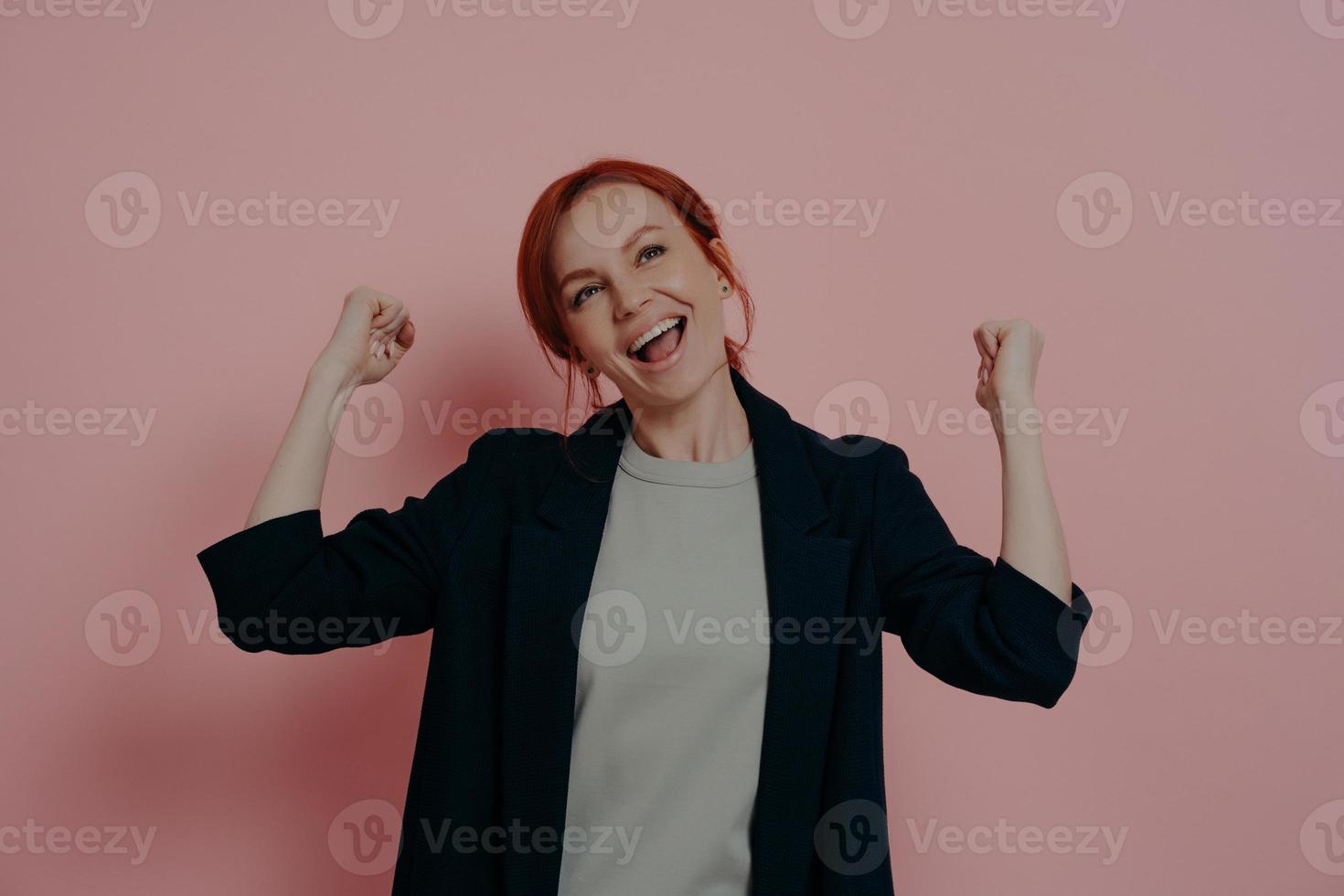 joven mujer de negocios de jengibre feliz y encantada levantando las manos en puños y celebrando el triunfo foto