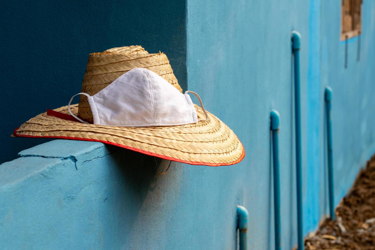 Woven bamboo hat of the farmer with a mask on a concrete wall blue. photo