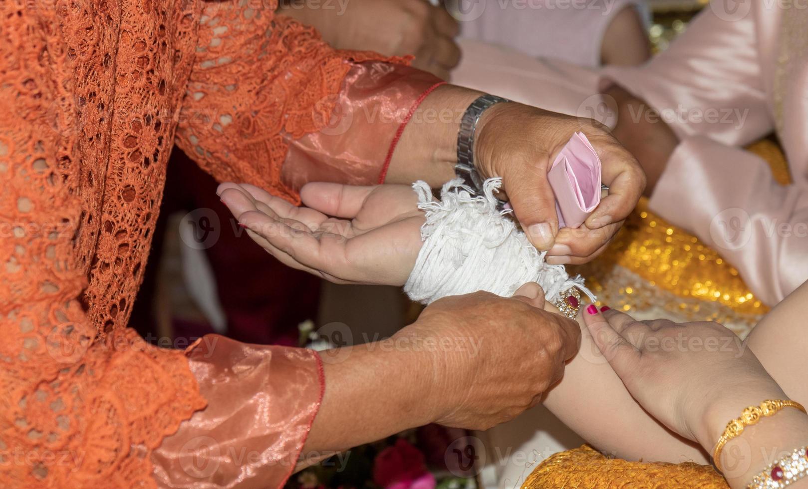 The elderly hand tied the thread to the bride. photo