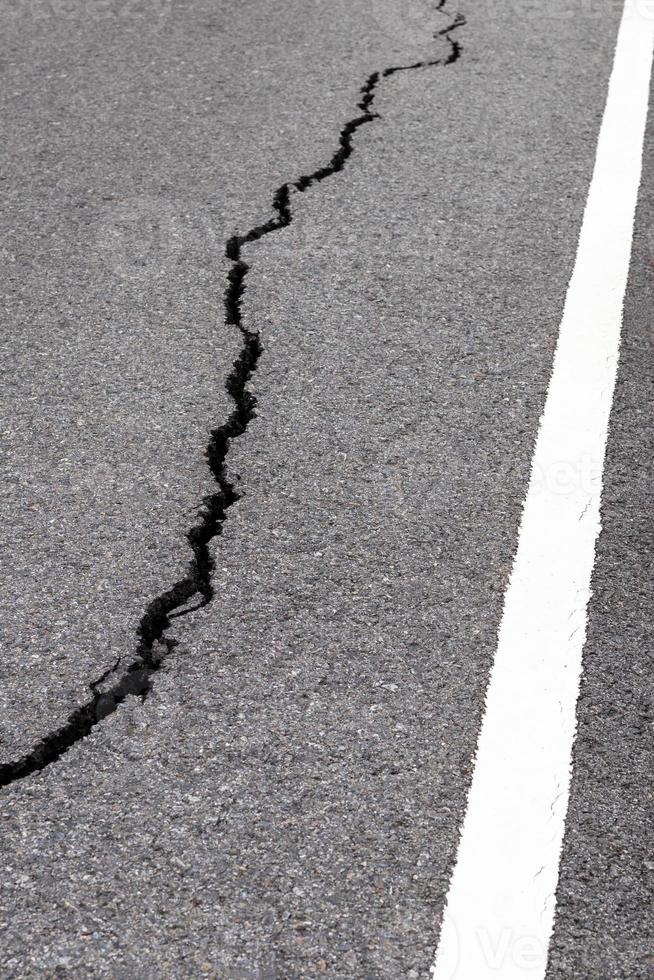 Surface cracks paved rural road near the white line. photo