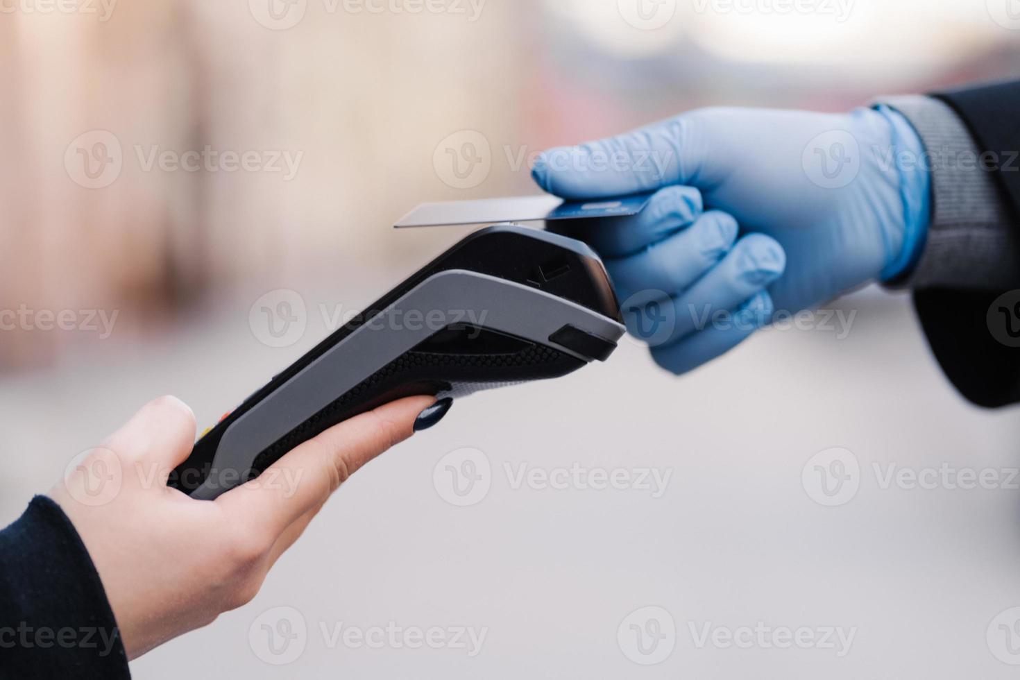 pago sin efectivo durante la cuarentena. mano en guantes de goma, tarjeta de crédito y terminal de pago. prevención de la propagación del coronavirus. buen servicio durante la situación de pandemia. tiro horizontal. COVID-19 foto