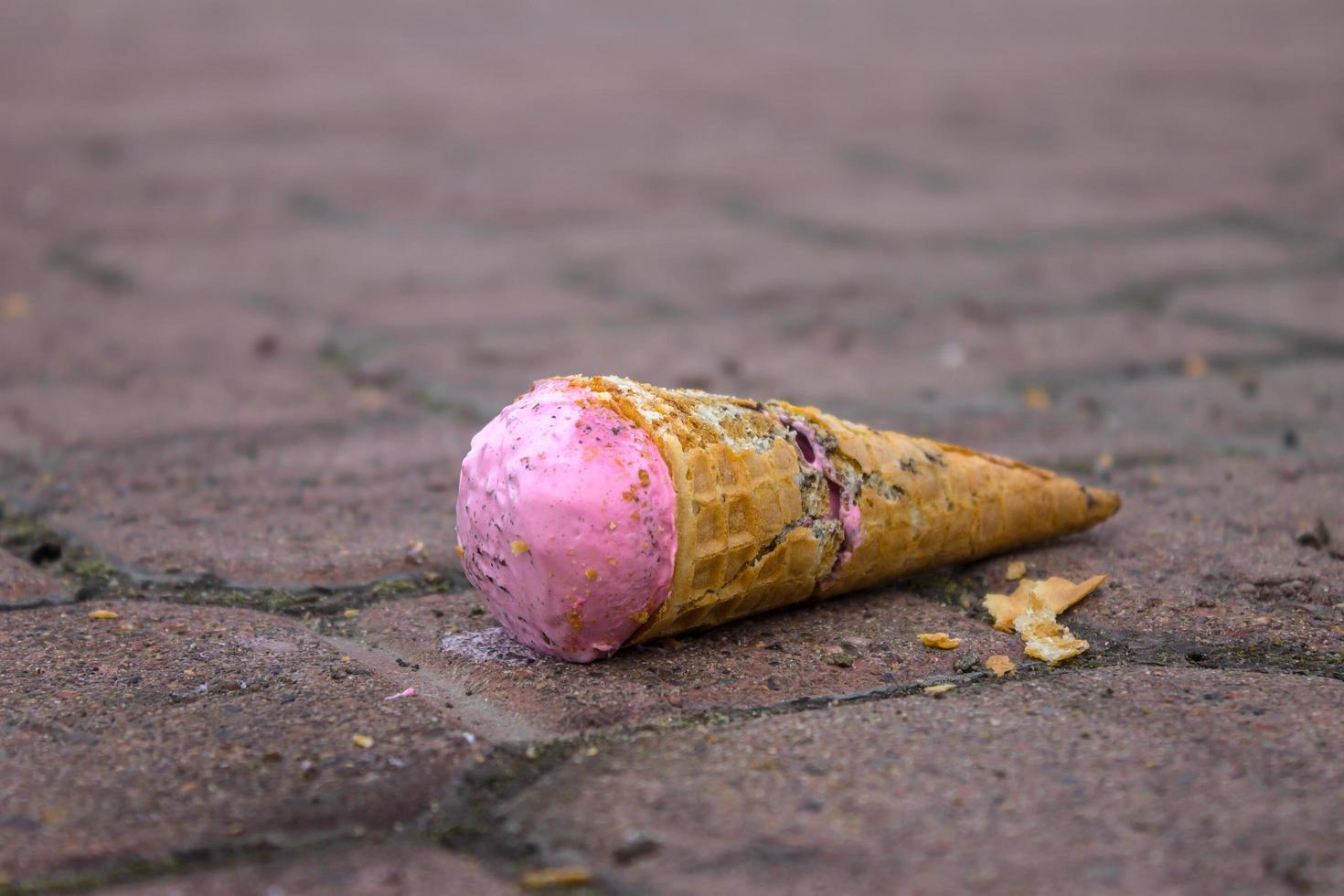 helado de fresa cayendo en una acera de la calle y un cono de gofre roto foto