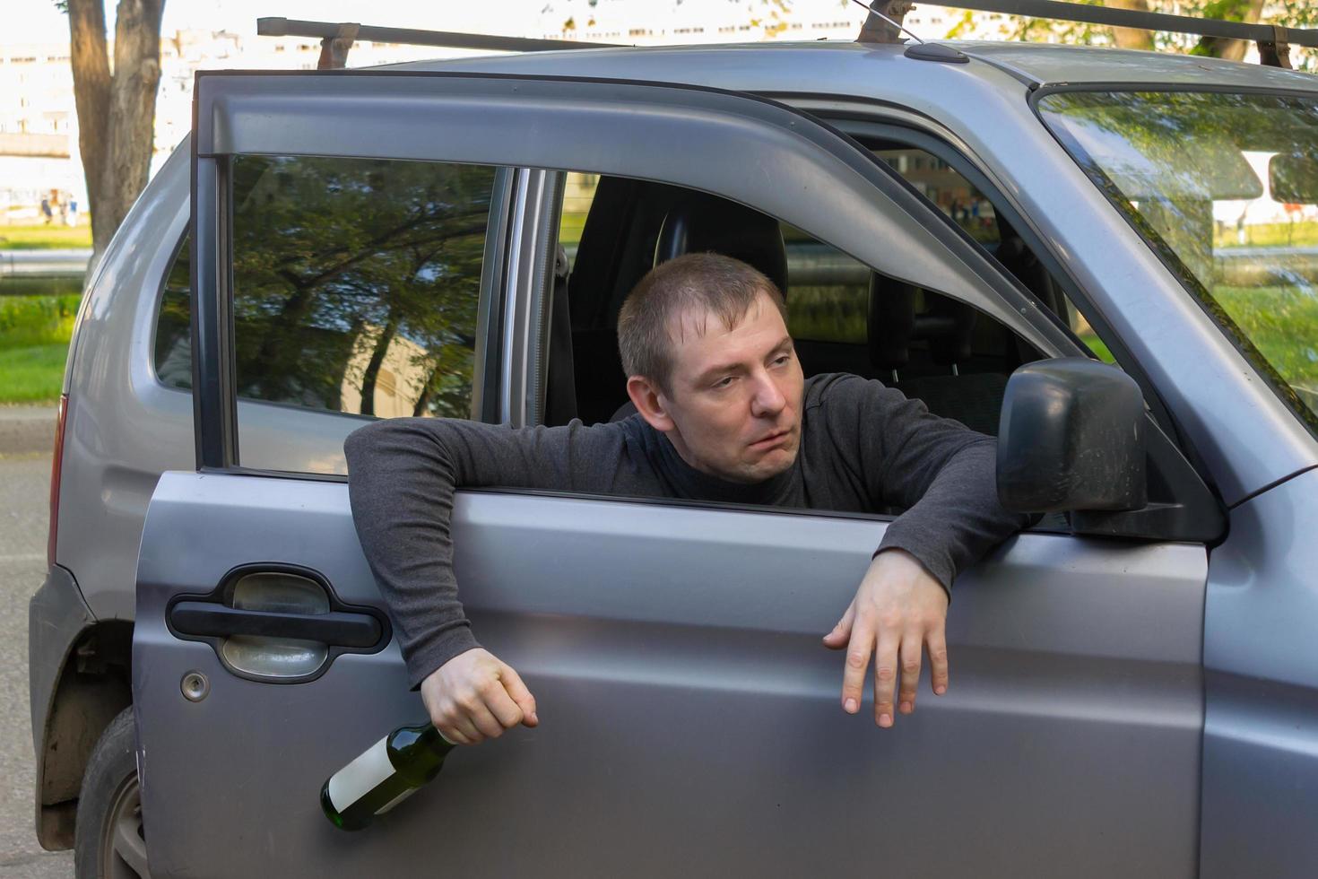 Drunk driver with a bottle of alcohol falls out of the door of his own car photo