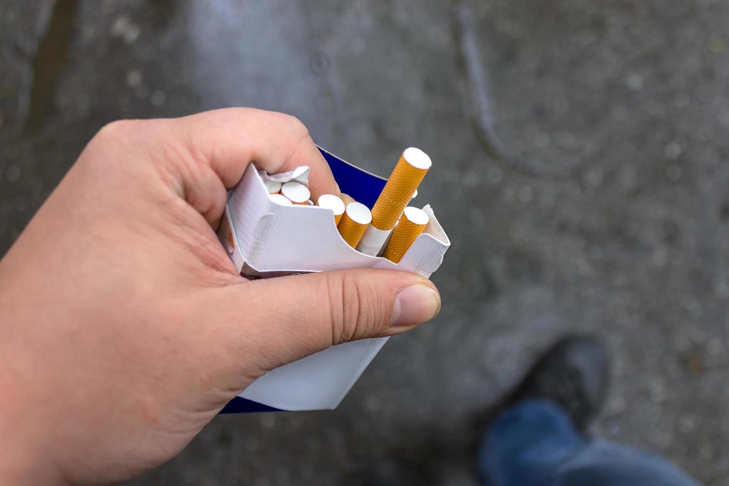 A pack of cigarettes in the hands of a smoker and an elongated cigarette photo