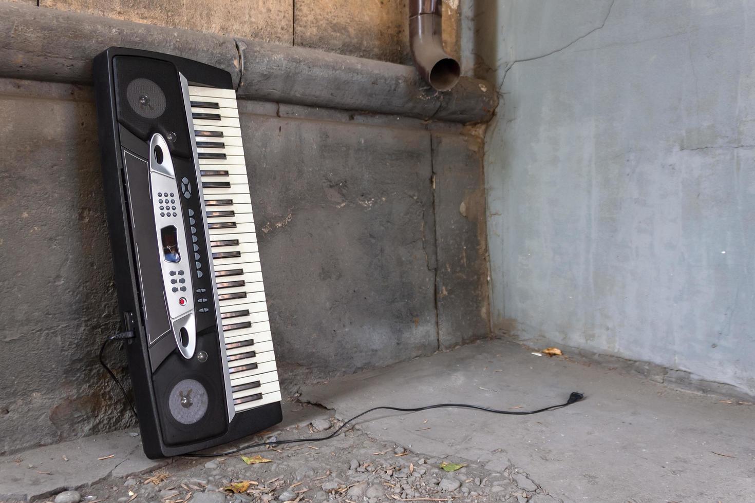 An abandoned old musical synthesizer stands near the wall of a building on the street photo