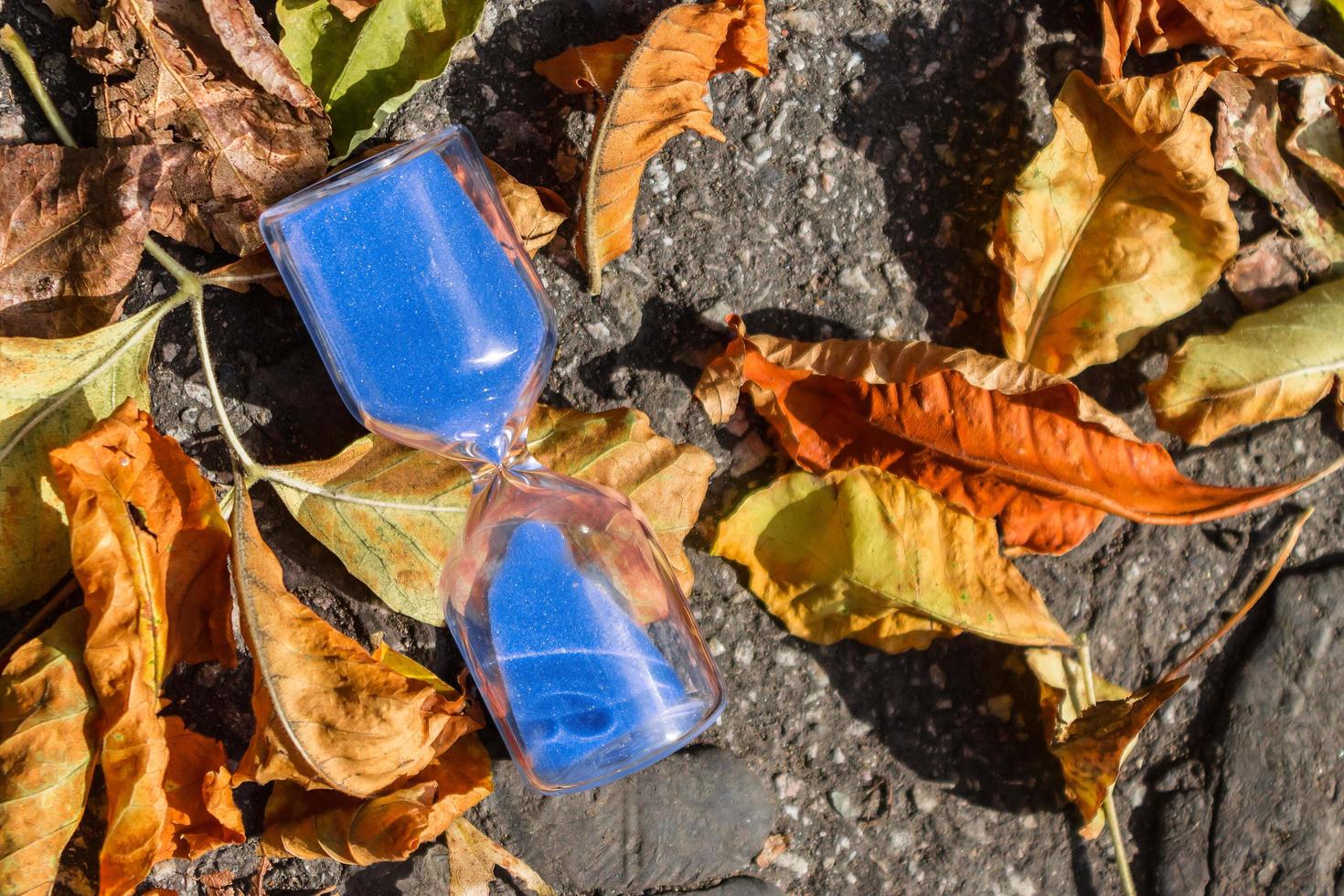 Hourglass on the pavement surrounded by autumn foliage photo