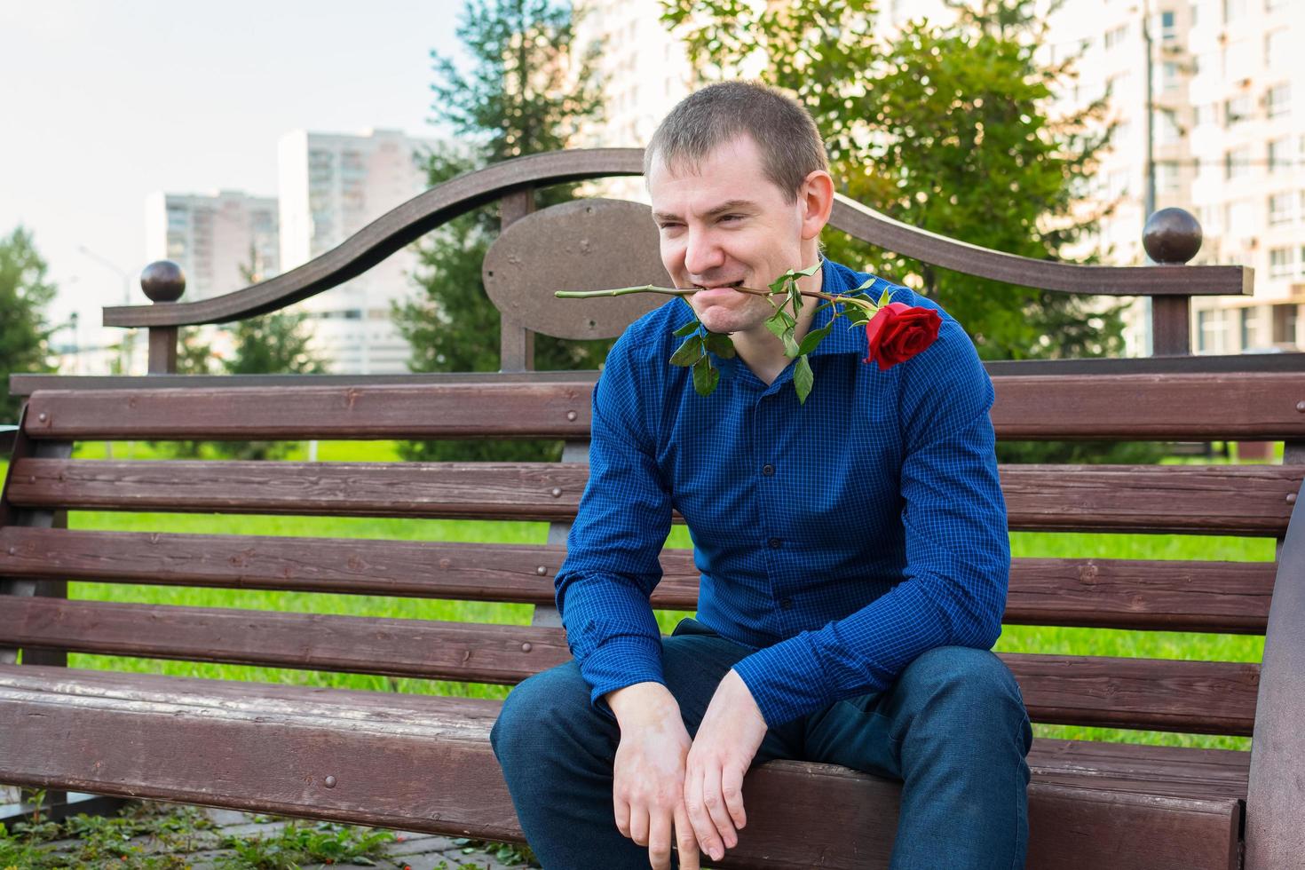 A man with a rose in his teeth sits on a park bench and looks at women photo