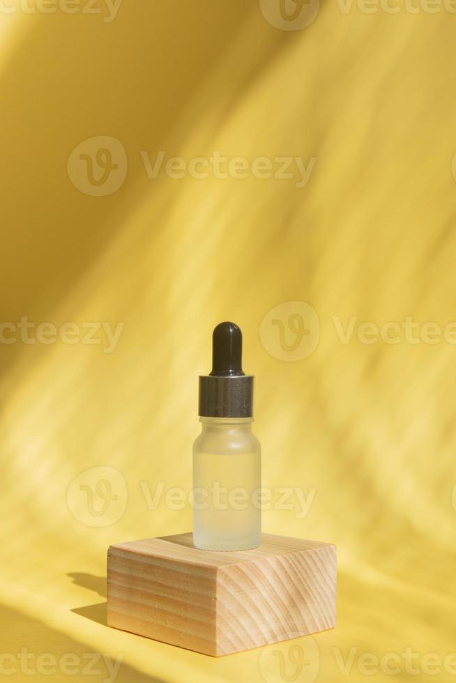 Glass bottle with a pipette on a wooden podium in the shade of blinds photo