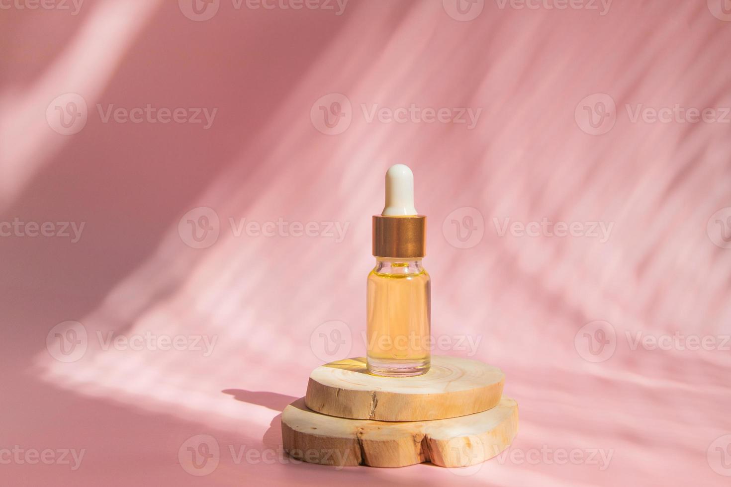 Glass bottle with a pipette on a wooden podium in the shade of blinds photo