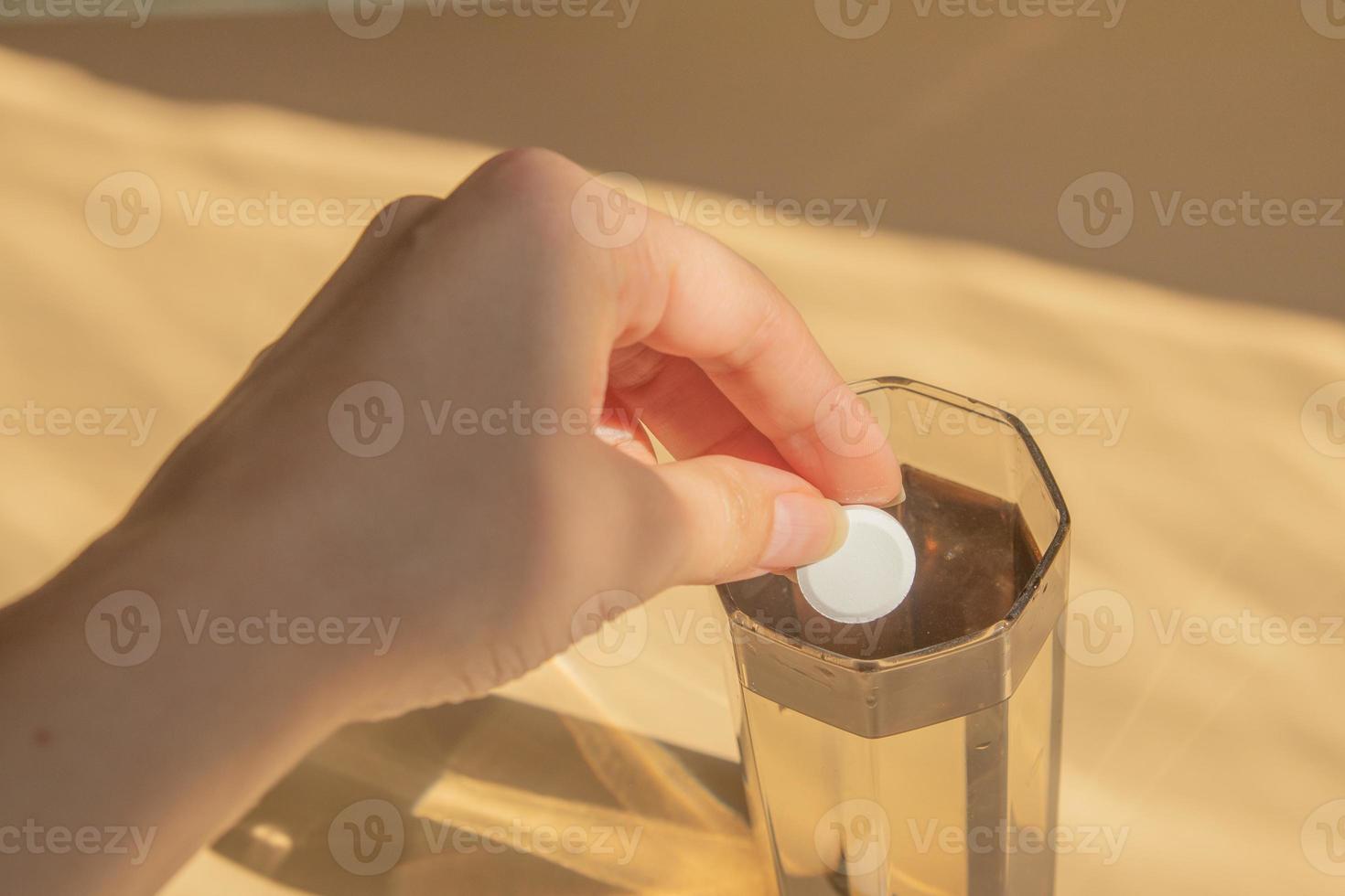 Female hand adds a tablet to a glass of water photo