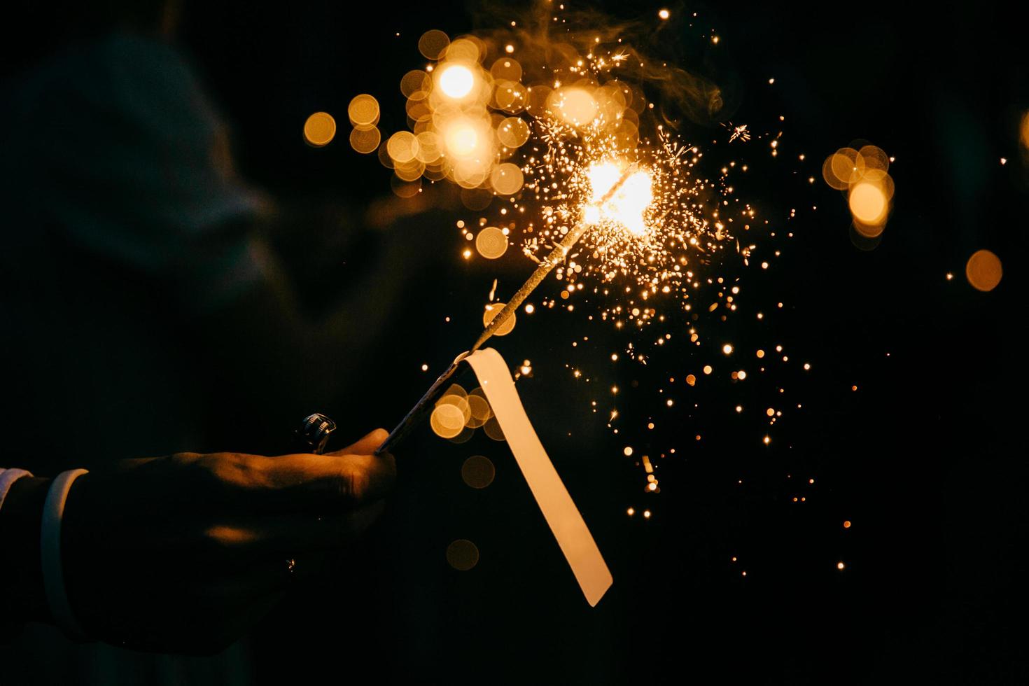 Bright festive sparkler in hand. Burning sparkle in darkness. Unrecognizable person holding glowing holiday sparkling hand fireworks, shining fire flame. Bengal fire against black background photo