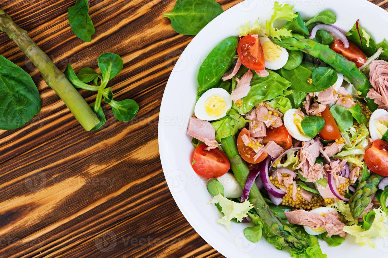 Salad with tuna, tomatoes, quail eggs, asparagus and onions on wooden background photo
