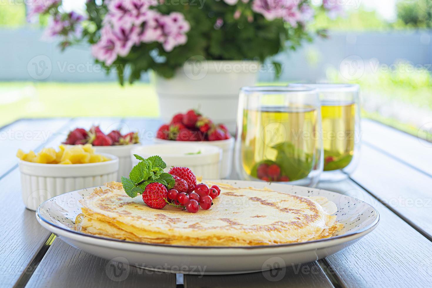 Pancakes with caramelized apples, raspberries, strawberries and red currants. Brunch with green tea and crepes. photo