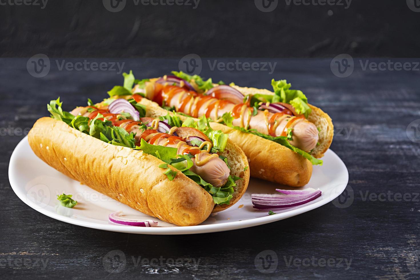 Homemade hot dog with sausage, salad, carrot, cucumber and tomato on wooden background photo