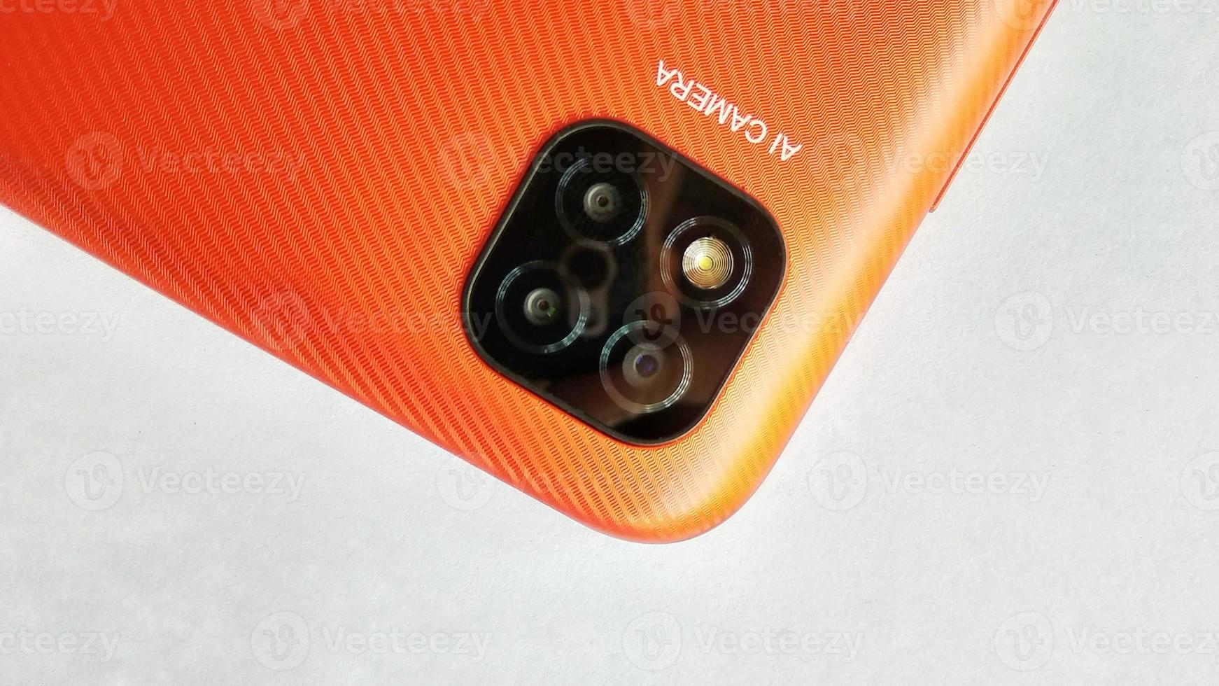 Orange smartphone with Artificial Intelligence cameras under white gray background. Suitable for company and industry advertising, poster, backdrop, promotion, tech company, etc. photo