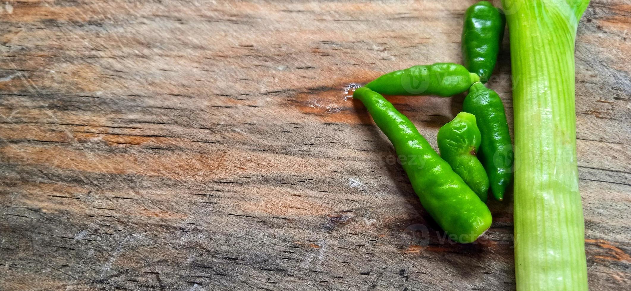 Vegetables of leek, garlic, and green chilli on the wooden cutting board. Vegetables ingredient background design. Suitable for advertising of food, drink, poster, backdrop, food company and industry. photo