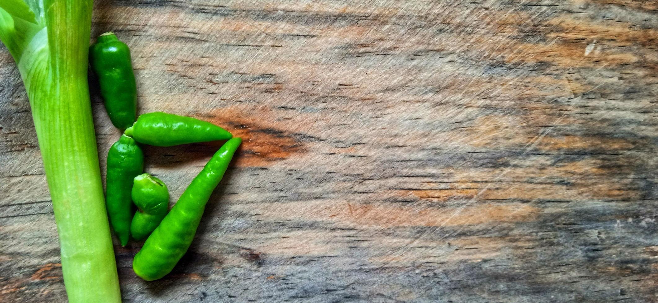Vegetables of leek, garlic, and green chilli on the wooden cutting board. Vegetables ingredient background design. Suitable for advertising of food, drink, poster, backdrop, food company and industry. photo