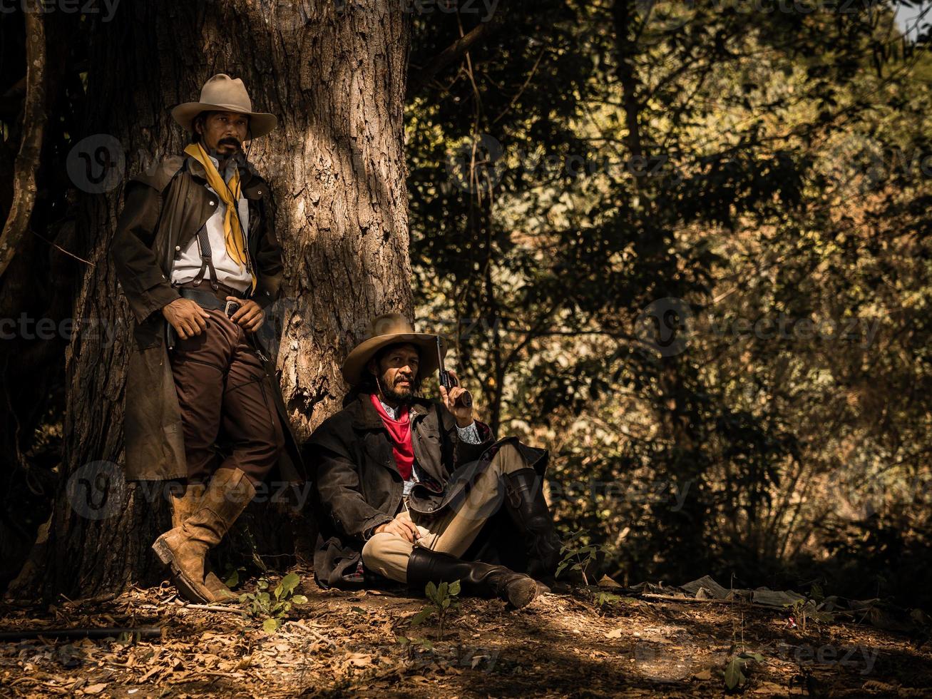 A twin senior cowboy stand and sat with a gun to guard the safety of the camp in the western area photo