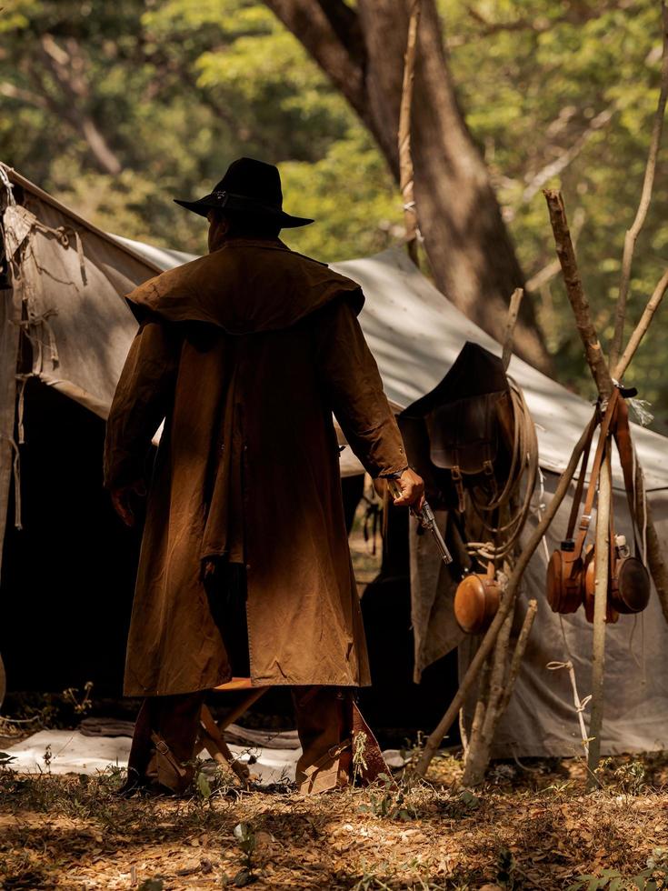 un vaquero mayor de pie con un arma para proteger la seguridad del campamento en el área occidental foto