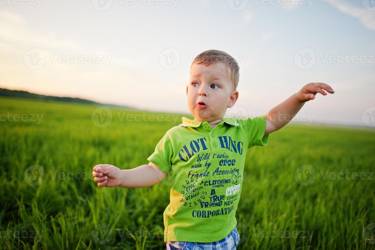 Cute boy in green grass field at evening. photo