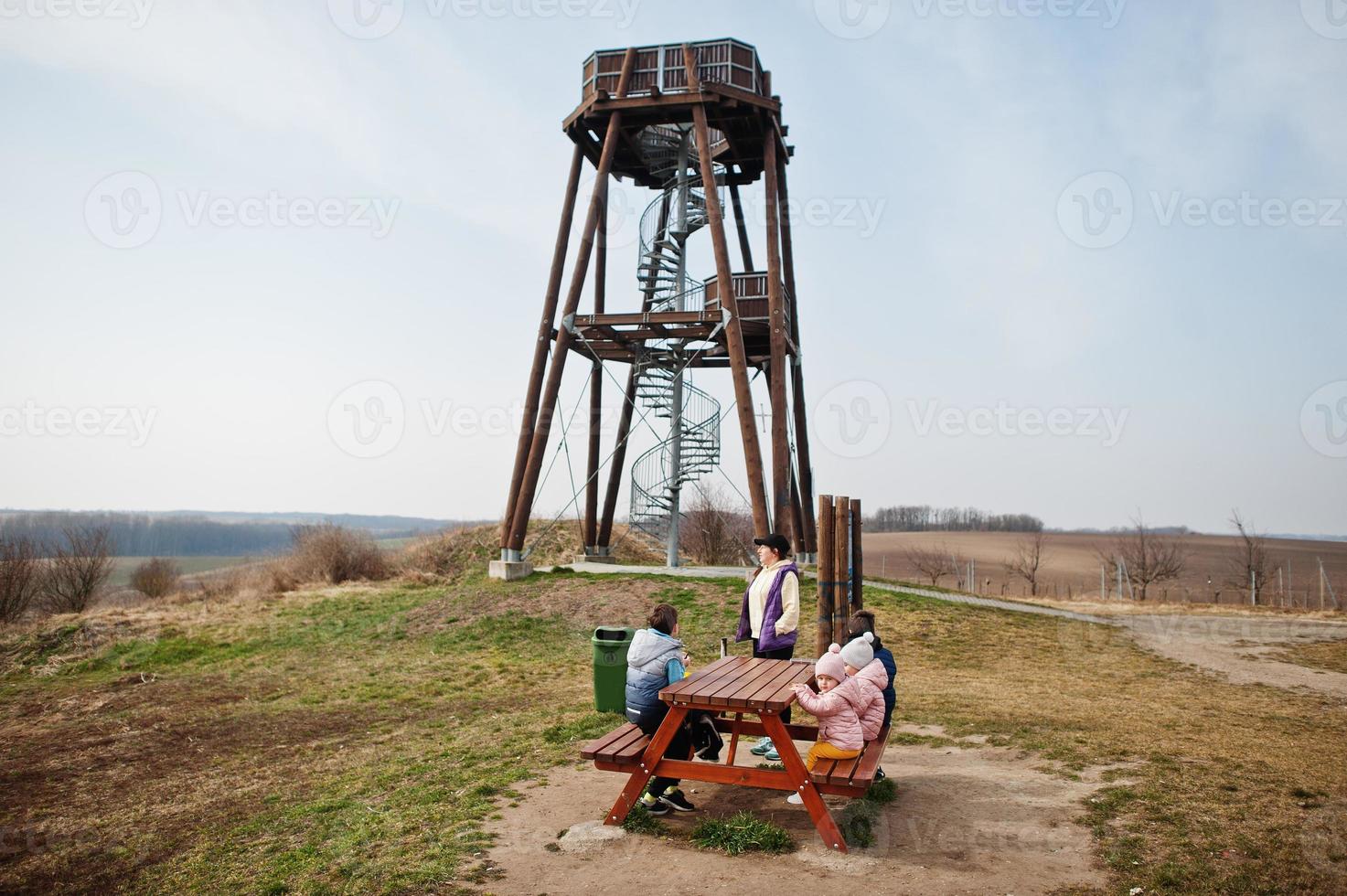 Mother with children sit at wooden table against observation tower. photo