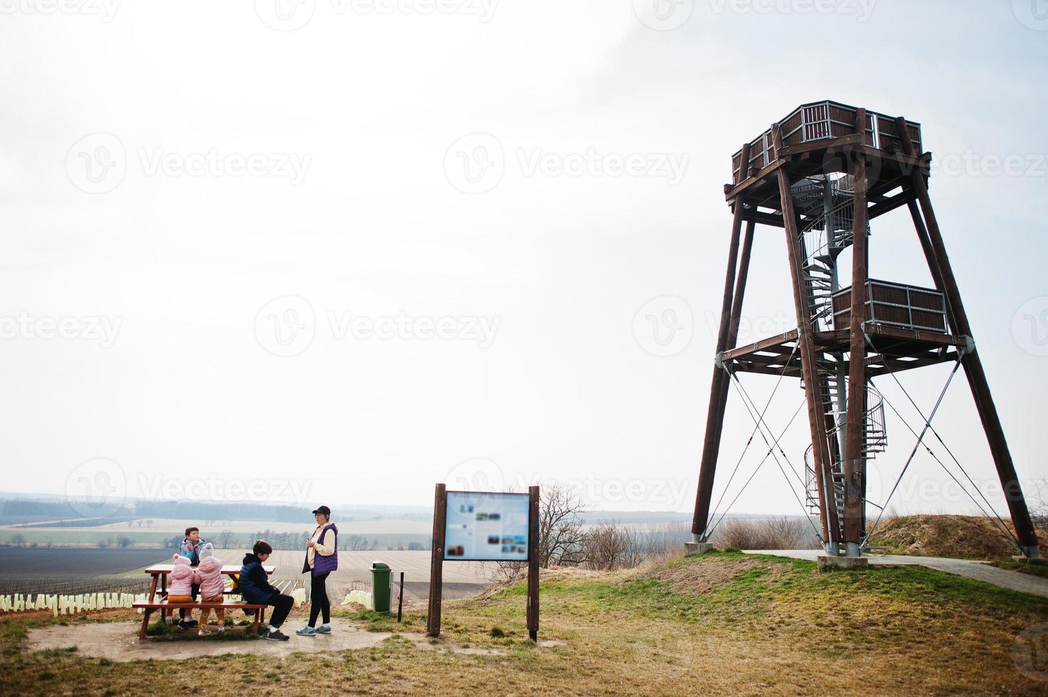 Mother with children sit at wooden table against observation tower. photo