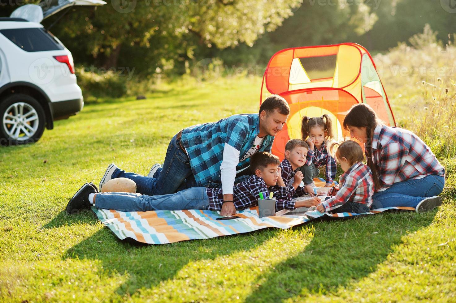 familia pasando tiempo juntos. cuatro niños y padres al aire libre en una manta de picnic. familia numerosa en camisas a cuadros. foto