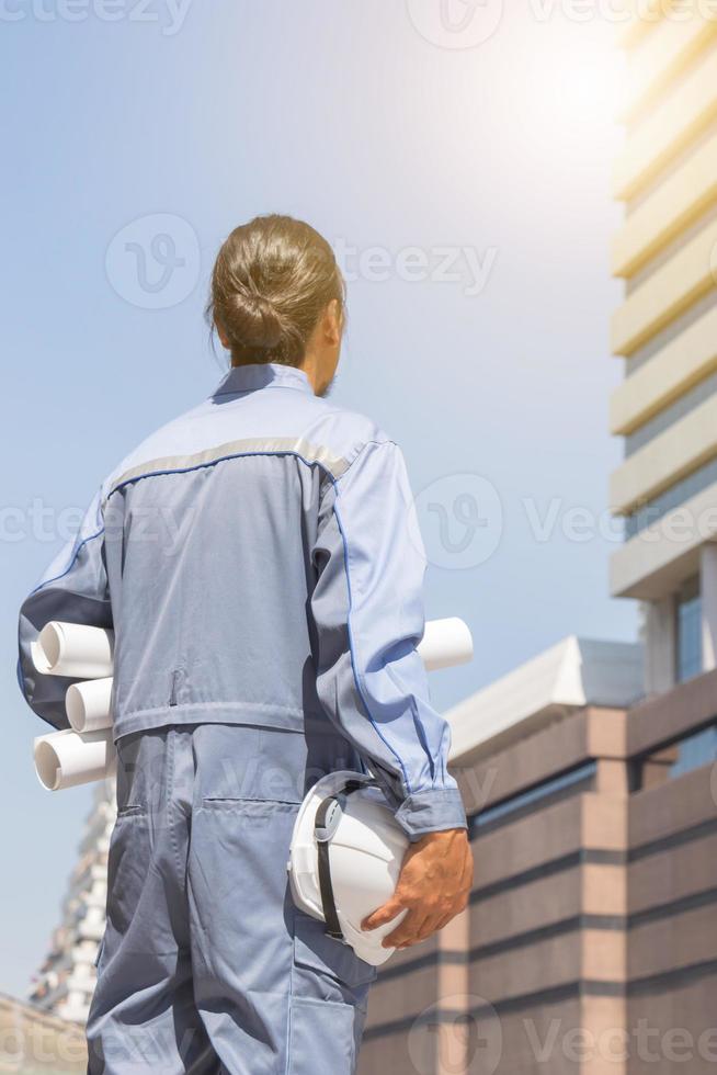 Engineer planing with white helmet and holding drawing paper in hand against city background planing and management concepts photo